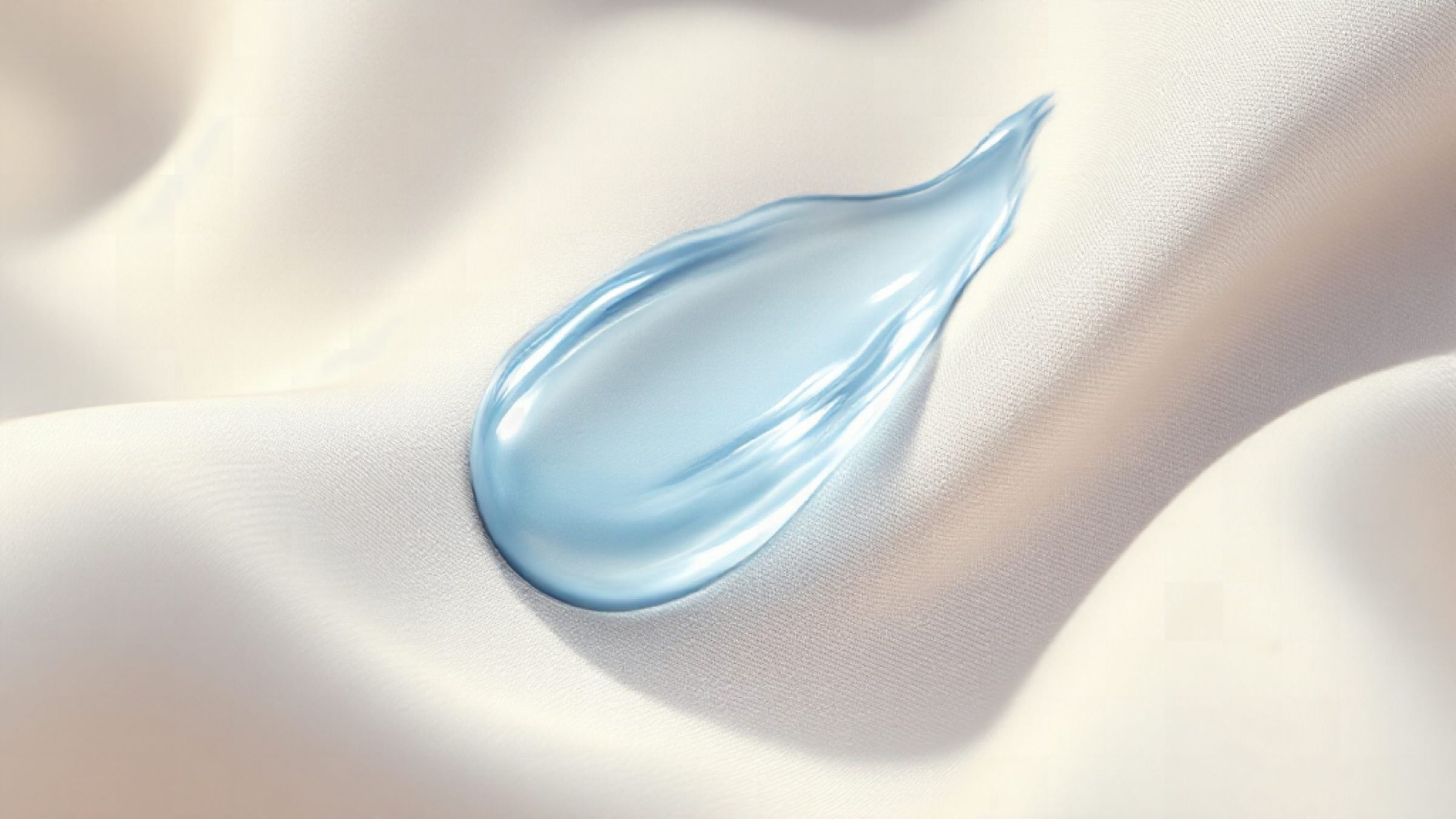 A swipe of pale blue serum resting on cream silk